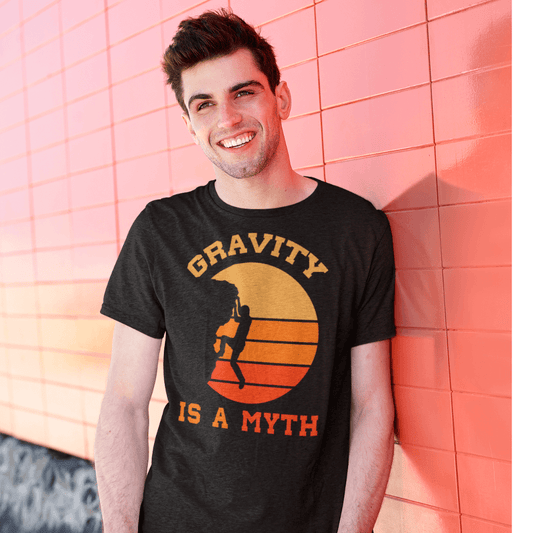 Man wearing "Gravity Is a Myth" climbing T-shirt with retro sunset graphic, standing against a vibrant orange wall.